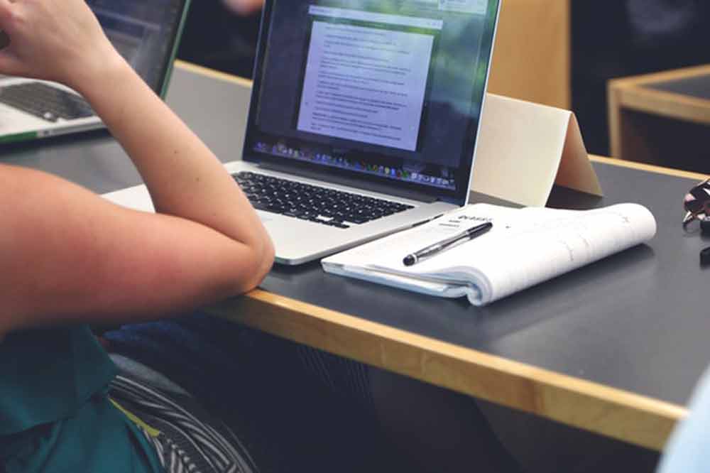 Ein Student in der Vorlesung mit Notizblock und Laptop. Mit den Notizen wird er die Vorlesung nachbereiten